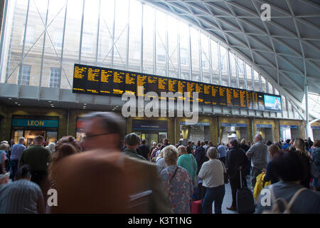 Persone in attesa nel piazzale di King's cross stazione ferroviaria guardando l'arrivo e partenze il pannello Informazioni Foto Stock