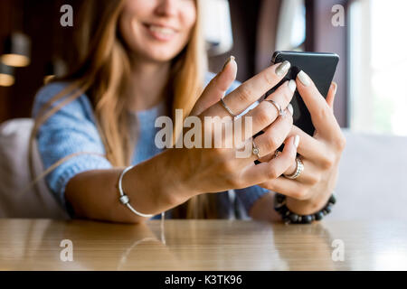 Close up le mani delle donne tenendo il telefono cellulare con la copia in bianco ghiaione dello spazio per la vostra pubblicità messaggio di testo o il contenuto promozionale, hipster ragazza guarda i video sul telefono cellulare durante la pausa caffè. Tonica. Messa a fuoco selettiva. Foto Stock