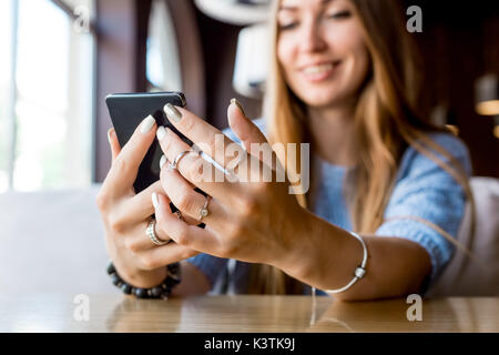 Close up le mani delle donne tenendo il telefono cellulare con la copia in bianco ghiaione dello spazio per la vostra pubblicità messaggio di testo o il contenuto promozionale, hipster ragazza guarda i video sul telefono cellulare durante la pausa caffè. Tonica. Messa a fuoco selettiva. Foto Stock