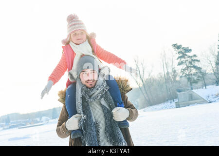 Padre dona piggyback ride a figlia nella neve Foto Stock