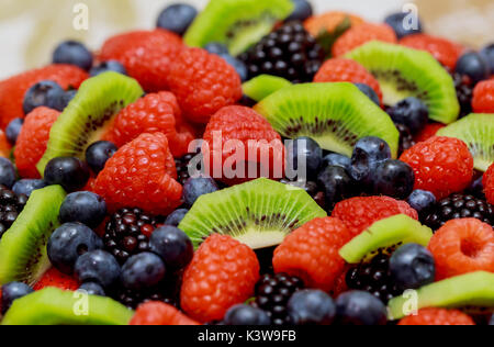 Torta di velluto con belle bacche fragole, lamponi mirtilli e menta giacente sulla carta argentata Foto Stock