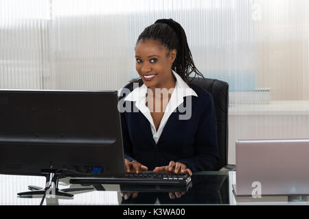 Sorridente giovane imprenditrice utilizzando computer in ufficio Foto Stock