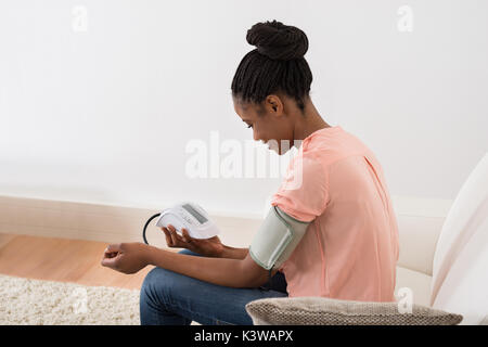 Giovane donna africana controllando la pressione del sangue a casa Foto Stock