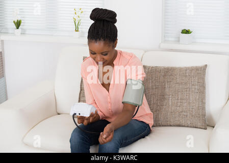 Giovane donna africana controllando la pressione del sangue a casa Foto Stock