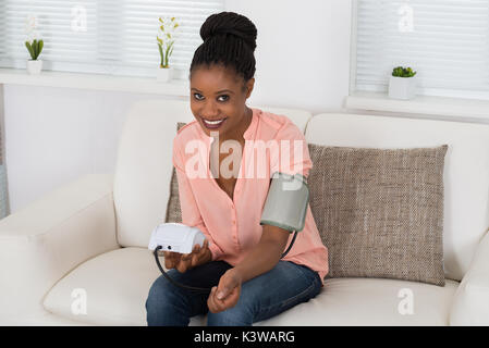 Giovane donna africana controllando la pressione del sangue a casa Foto Stock