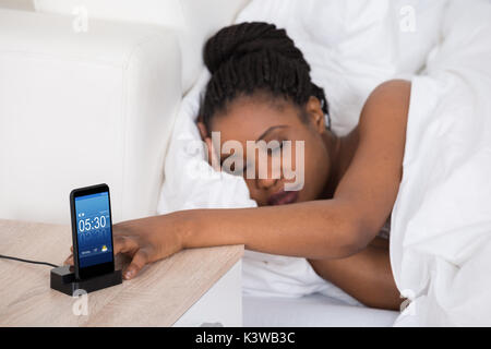 Giovane donna africana che dorme sul letto con allarme sul telefono cellulare Foto Stock