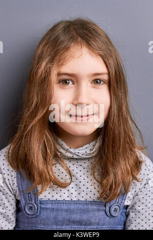 Studio shot della graziosa bambina. Affascinante marrone capelli bambina su sfondo grigio guardando la fotocamera. Concetto di childishness e bambini innocenza. Foto Stock