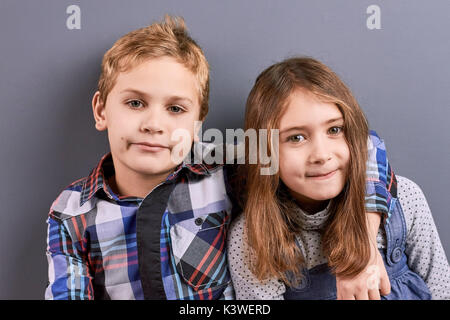 Ritratto di abbracciando i bambini. Carino coppia di ragazzi in abiti casual sono abbracciava, guardando la fotocamera su sfondo grigio. Foto Stock