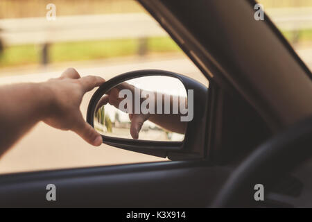 Mano d'uomo corregge gli specchi laterali in auto, tonificazione retrò. Foto Stock
