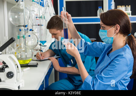 Giovane maschio e femmina gli scienziati in uniforme facendo alcune ricerche in un laboratorio. Assistenza sanitaria e il concetto di biotecnologia Foto Stock