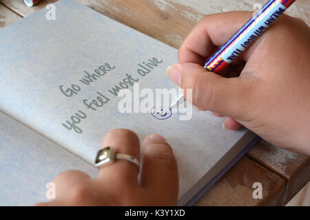 La donna il disegno di una faccina sorridente in un giornale aperto a una pagina con il mantra andare dove ti senti più vivo Foto Stock