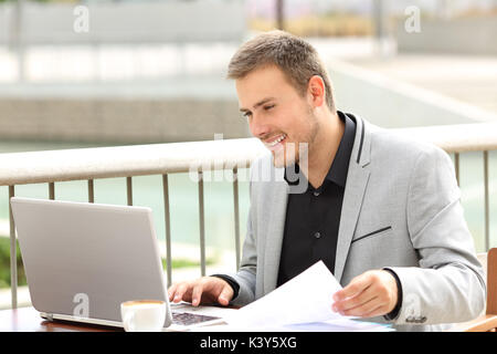 Singola executive smiley lavorare on line con un portatile seduti in un caffè Foto Stock