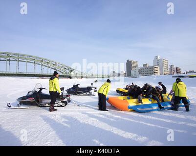 I visitatori si divertono con banana boat sul ghiaccio tirato dalla neve mobile all'Asahikawa Winter Festival, Hokkaido, Giappone Foto Stock