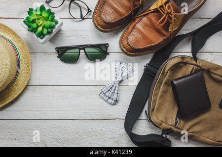 Vista superiore accessori per viaggiare con abbigliamento uomo concetto. Il filtro bow tie,wallet su sfondo di legno.guarda,occhiali da sole,bag,hat,cinghia e scarpe sulla tavola di legno. Foto Stock