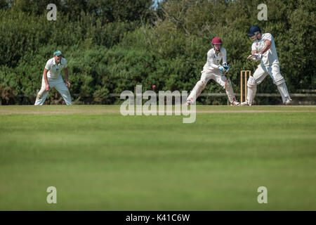 Un battitore gioca un colpo durante una domenica League match tra due locali squadre di cricket. Foto Stock