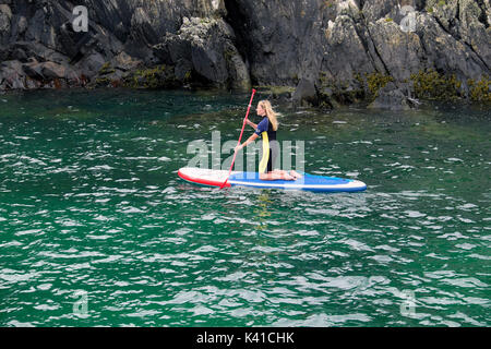 Una donna in una muta paddleboarding nel porto Porthclais verso St Brides baia sulla costa in estate vicino a St David's West Wales UK KATHY DEWITT Foto Stock