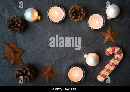 Rustico decorazioni di Natale e le luci del tè in pietra scura superficie con copia spazio nel centro. visto dal direttamente sopra Foto Stock
