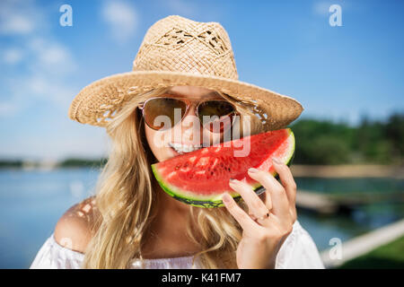 Una foto di una giovane donna felice di mordere un pezzo di cocomero. Foto Stock