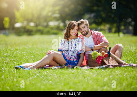 Una foto di giovani, felice coppia avente un picnic al parco. Essi stanno sorridendo felicemente. Foto Stock