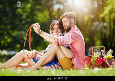 Una foto di una coppia giovane picnic al parco. Essi stanno prendendo loro stessi una foto. Foto Stock