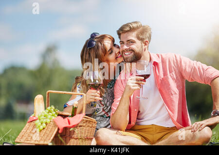 Una foto di una giovane coppia felice picnic al parco. Stanno bevendo vino e flirtare. Foto Stock