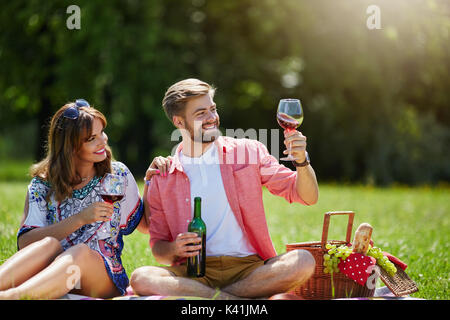 Una foto di una coppia giovane tenendo rilassarsi nel pomeriggio picnic. Si sta cercando un po' di vino rosso. Foto Stock