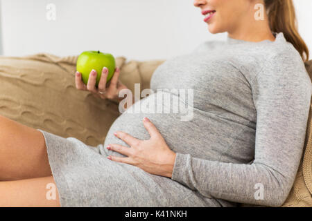 Felice donna incinta mangiare mela verde a casa Foto Stock