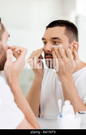 Giovane uomo di applicare la crema per il viso a bagno Foto Stock