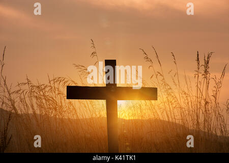 Una croce cristiana silhouette su sfondo al tramonto Foto Stock