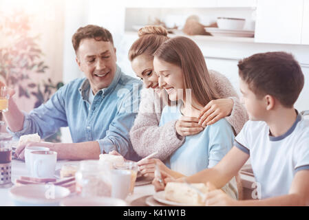 Madre sentimentale abbracciando la figlia durante la colazione in famiglia Foto Stock