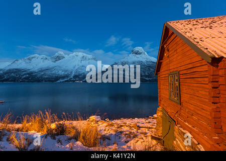 Cabina in legno del pescatore illuminato circondato dal mare ghiacciato al crepuscolo Storfjorden Lapponia Alpi Lyngen Tromsø Norvegia Europa Foto Stock