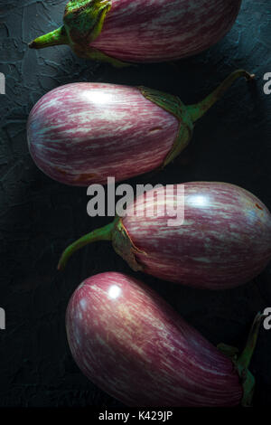 Le melanzane in striato con rami su una scura pietra grigia close-up verticale Foto Stock