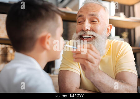 Allegro senior uomo mettere un puntino di vernice su nipoti naso Foto Stock