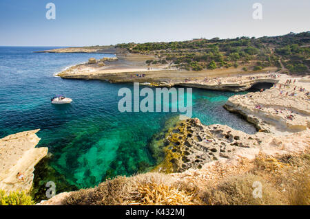 San Pietro piscina in estate nei pressi di Marsaxlokk, Malta - piscina naturale un ampio angolo di visione, con una barca a motore, turisti godendo dell'ambiente Foto Stock