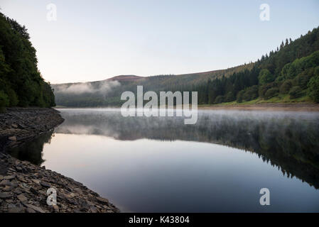 Incredibile settembre mattina al serbatoio Ladybower, Peak District, Derbyshire, in Inghilterra. Drifting di nebbia al di sopra della superficie dell'acqua. Foto Stock
