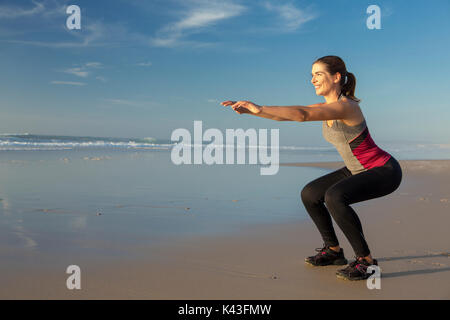 Riprese di una bella donna che fa squat esercizi in spiaggia Foto Stock