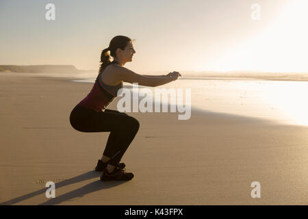 Riprese di una bella donna che fa squat esercizi in spiaggia Foto Stock