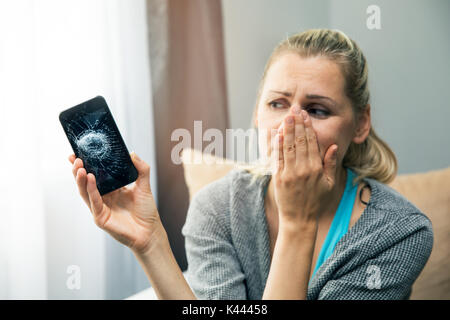 Triste donna azienda smart phone con schermo rotto in mano Foto Stock