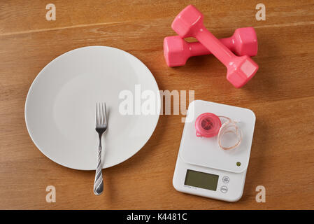 Alimento bianco bilance con tapeline rosa, una piastra con forcella e manubri su una tavola di legno Foto Stock
