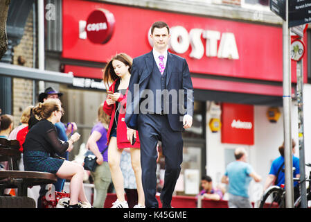 Bianco giovane imprenditore inglese passeggiate attraverso un trafficato centro cittadino con il pubblico in generale in background e vicino alla zona dello shopping Foto Stock