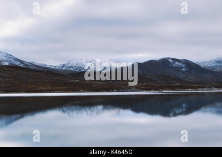 Montagne dalle vette innevate riflettente nel lago Bygdin. Da Jotunheimen Norvegia Foto Stock