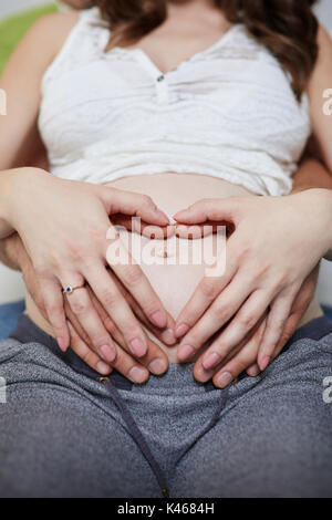 Ritratto verticale della donna incinta e il suo uomo tenendo le mani sul suo ventre nel gesto di amore. Foto Stock