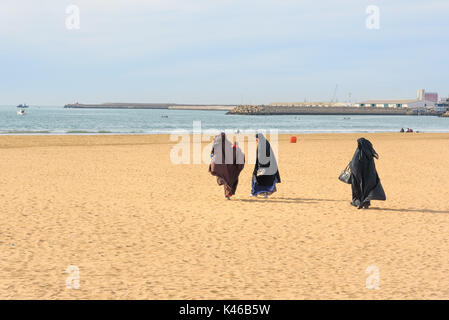 Agadir. Marocco - 23 dicembre 2016: Le donne musulmane in nero camici lunghe passeggiate sulla spiaggia Foto Stock