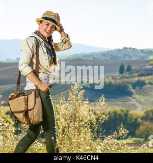 Alla scoperta di magiche vedute della Toscana. Ritratto di sorridente donna attiva escursionista in hat godendo di vista in Toscana Foto Stock