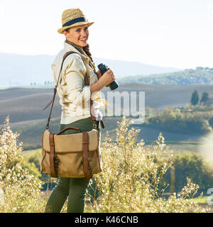 Alla scoperta di magiche vedute della Toscana. sorridente donna avventura escursionista in hat escursioni in Toscana con un binocolo Foto Stock