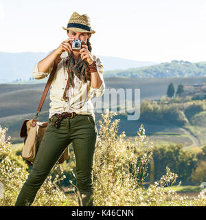 Alla scoperta di magiche vedute della Toscana. donna sana escursionista con borsa trekking in Toscana prendendo foto con vintage fotocamera foto Foto Stock