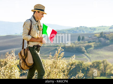 Alla scoperta di magiche vedute della Toscana. sorridente donna avventura escursionista in hat con bandiera italiana gode di vista in Toscana Foto Stock