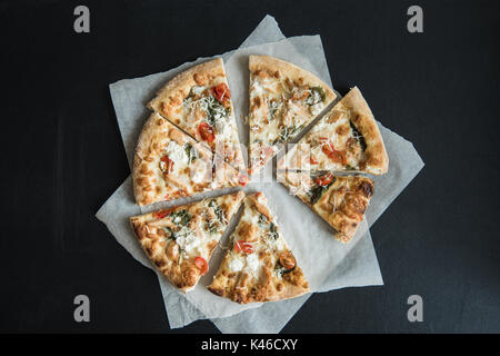 Vista superiore della tradizionale italiano pizza a fette su pergamena sulla superficie scura Foto Stock