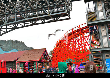 Seagull volo sopra l'apparente caos del Pleasure Beach parco divertimenti in una piovosa giornata d'estate,Blackpool, Lancashire, Regno Unito Foto Stock