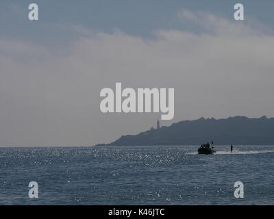 Una femmina waterskiier e velocità barca sul mare con punto di partenza il faro in background, in south devon Foto Stock